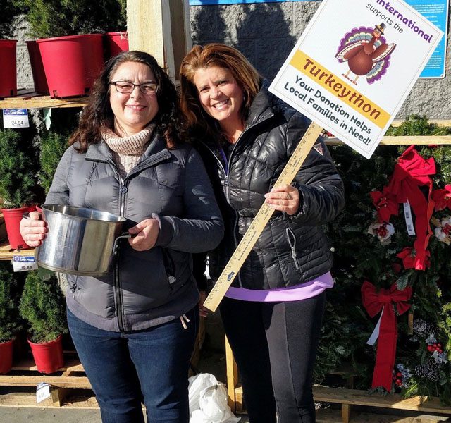 About Our Agency - Portrait of Two Smiling Helwig Insurance Staff Members Standing Outside a Store Holding a Turkeython Donation Sign