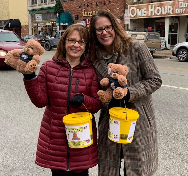 About Our Agency - Portrait of Two Smiling Helwig Insurance Team Members Standing on the Street with Donation Buckets and Teddy Bears