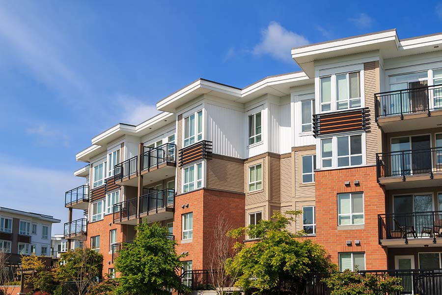 Condo Building Insurance - View of a Modern Brick Apartment Building with Green Trees in the Front Against a Bright Blue Sky